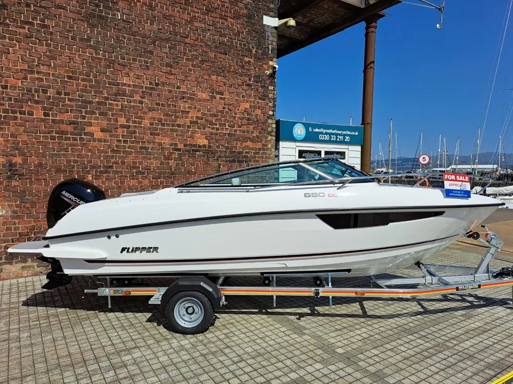White Flipper 650 DC boat on a trailer for sale, parked near a brick wall with a marina and sign in the background.